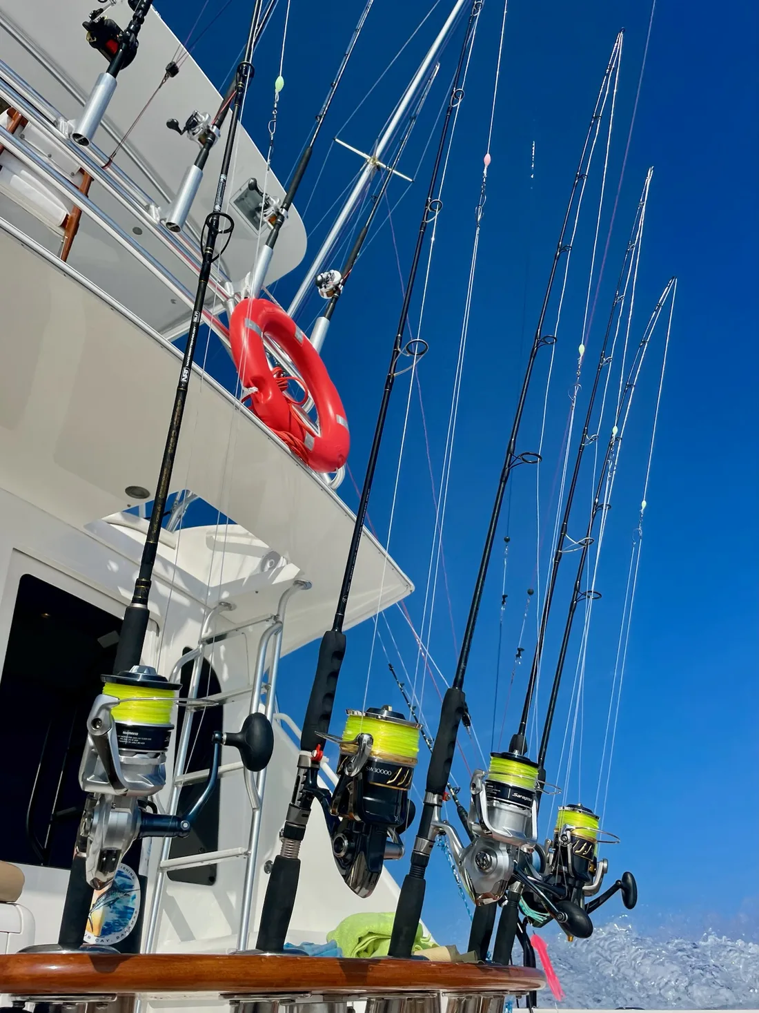 Upward view of four spinning reels spooled with bright yellow fishing line, rods fanned against a deep blue sky aboard a moving sport-fishing boat.