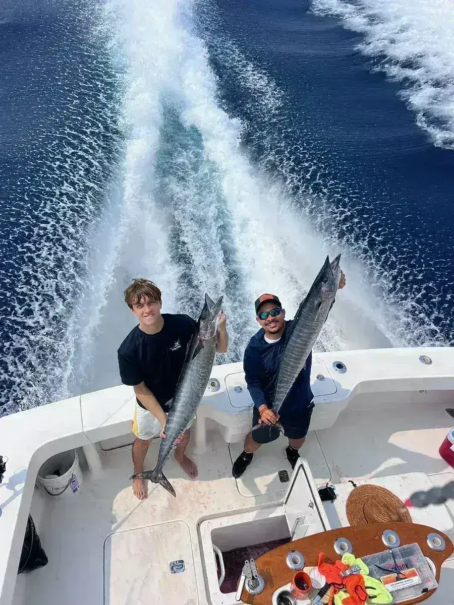 Two crew members holding a wahoo on the deck of the Vuelto Loco